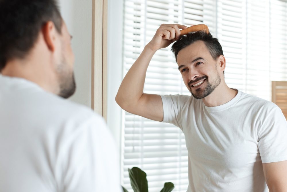 Handsome,Man,Styling,His,Hair,With,Comb,Near,Mirror,At Un homme admire le résultat de son traitement PRP contre la perte de cheveux